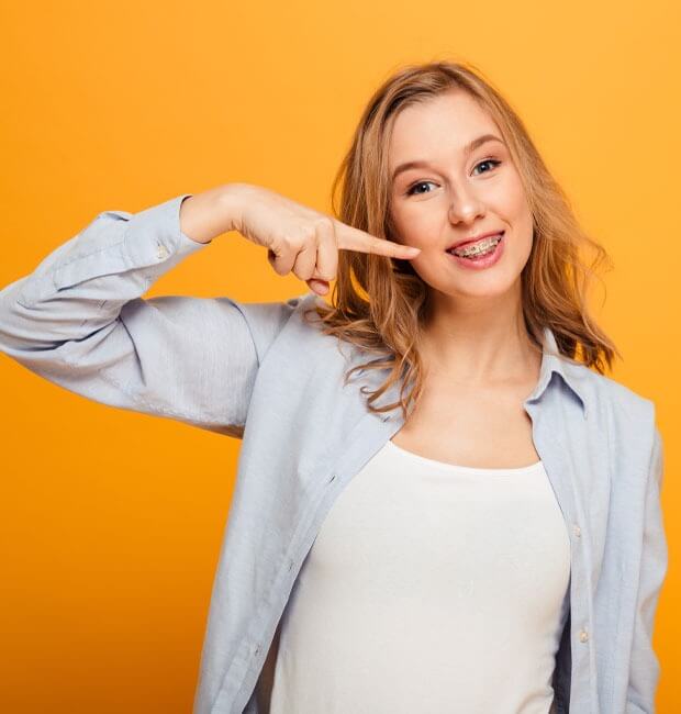 A teen girl smiling and pointing at her braces