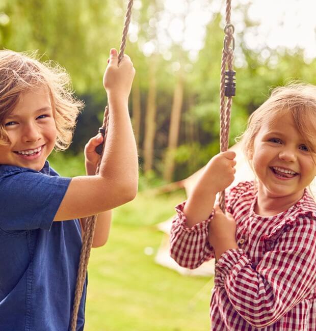 Two smiling children playing on swings in a playground