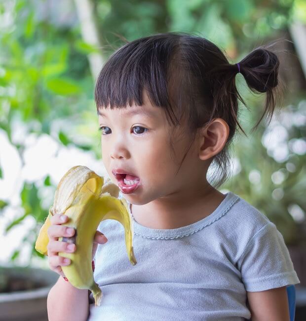 A young asian girl eating a banana in the park