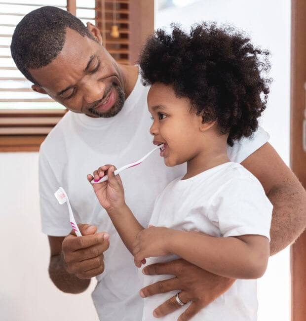 A father with his son teaching him how to brush his teeth correctly